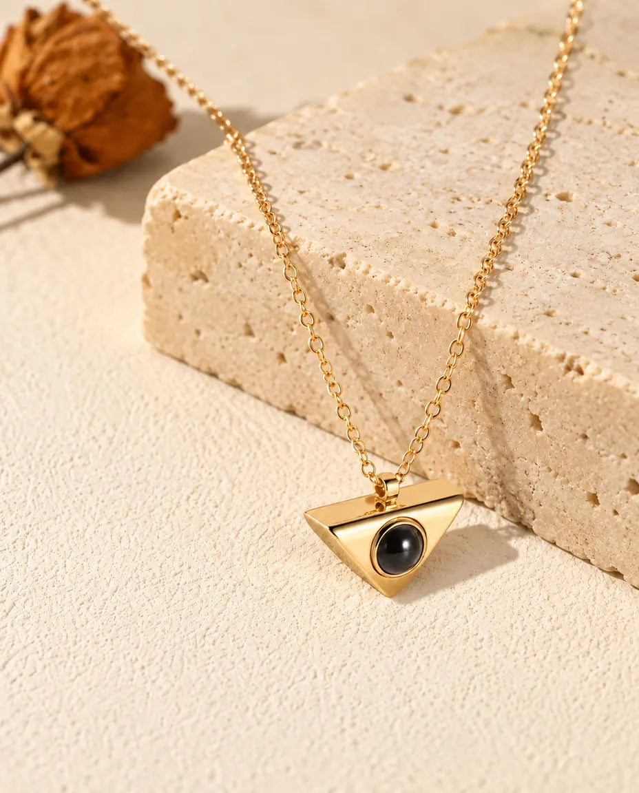 Gold tone triangle projection necklace hanging over a travertine block