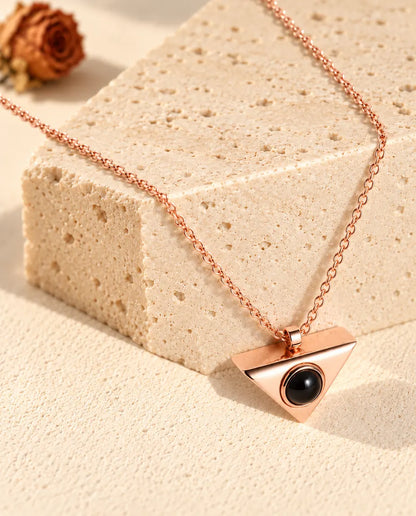 Rose gold tone triangle projection necklace hanging over a travertine block