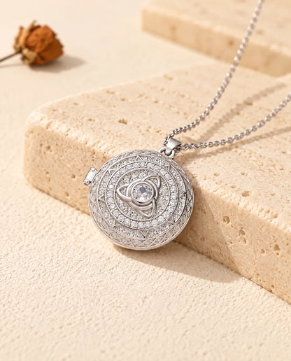 Personalised round trinity knot photo locket necklace in silver tone with cubic zirconia, resting on a travertine block