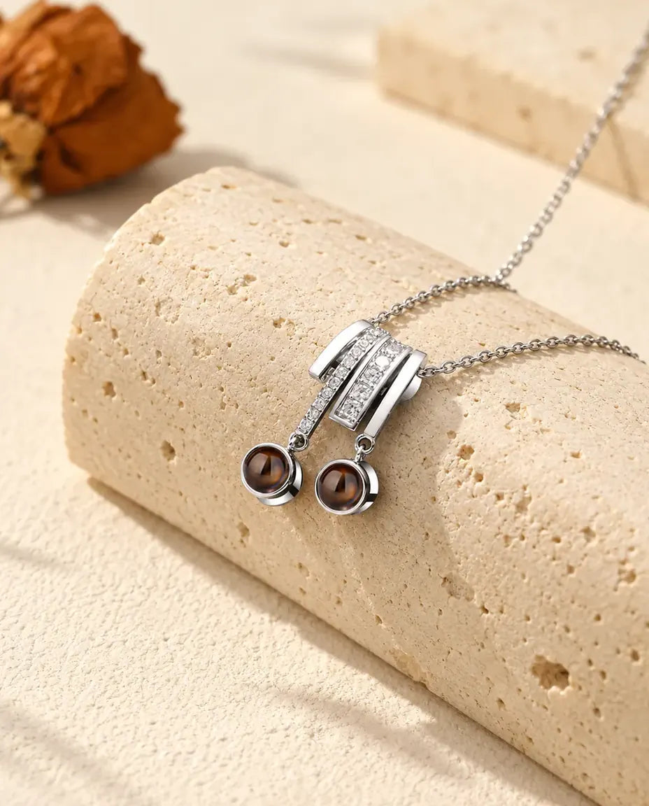 Personalised two photo projection necklace in silver tone with a pave slide and two brown projection stones on a travertine block