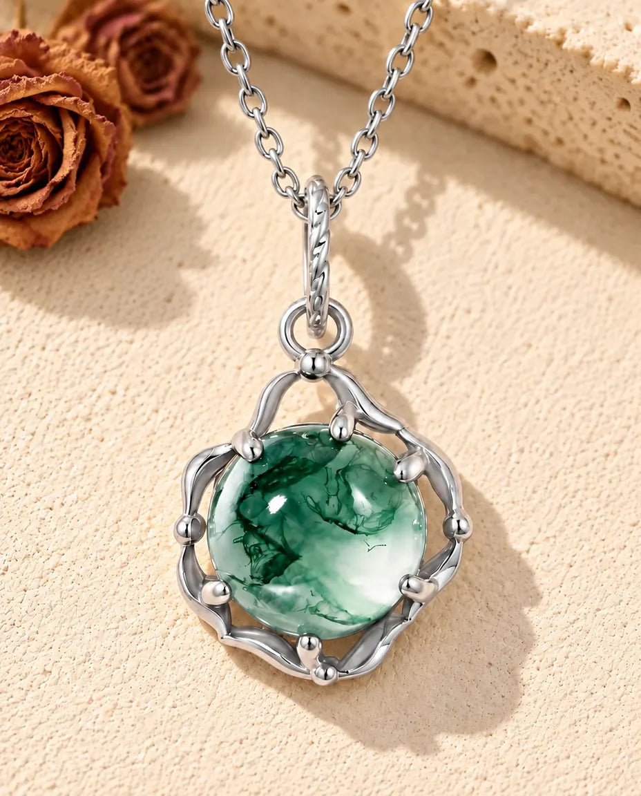 Round Moss Agate Cage Necklace in 925 Sterling Silver - lying on a cream textured surface beside a travertine block