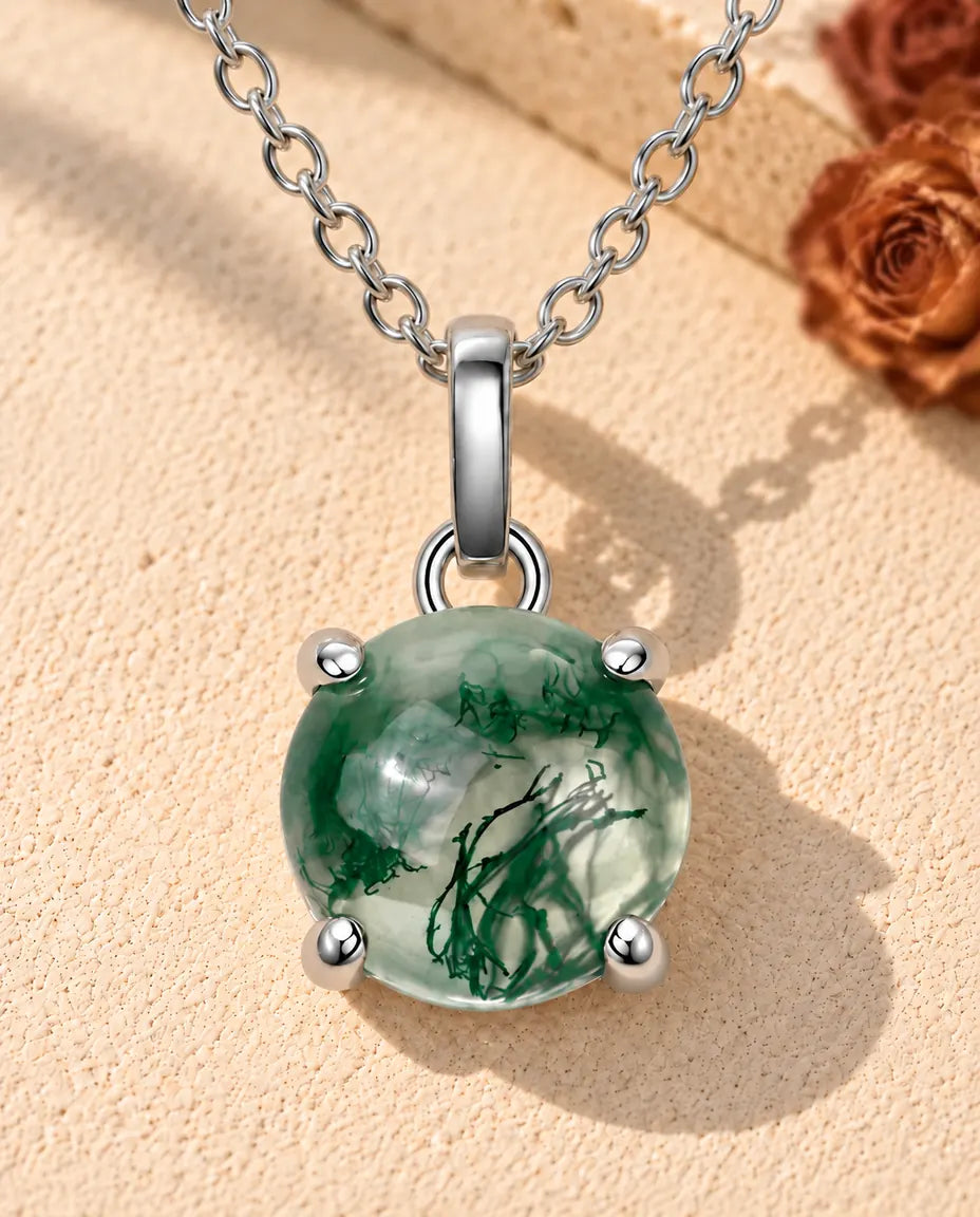 Round Moss Agate Solitaire Necklace in 925 Sterling Silver - lying on a cream textured surface beside a travertine block