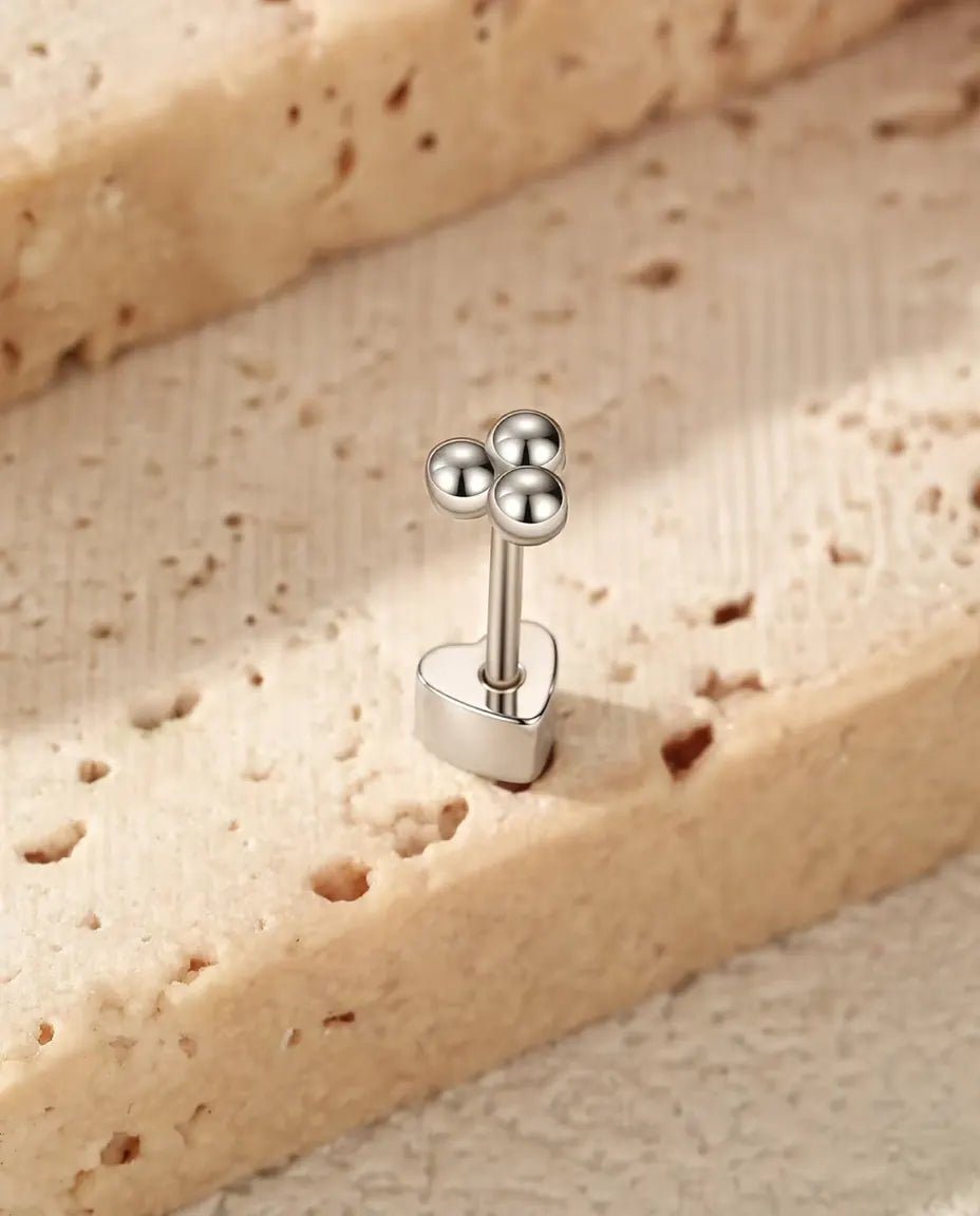 Silver Ball Trefoil Stud Earrings in 925 Sterling Silver - standing upright on its heart-shaped back on a cream textured surface