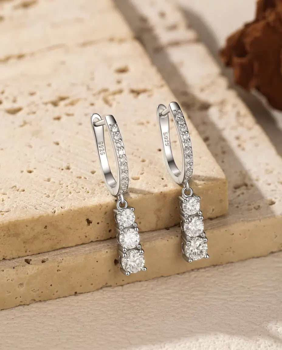 Three Stone Moissanite Drop Hoop Earrings in 925 Sterling Silver - pair hanging from the edge of a travertine slab